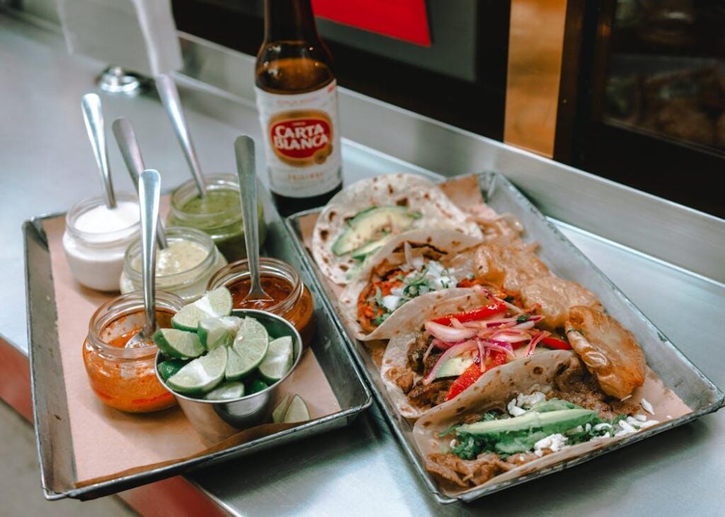 A tray of assorted tacos served with fresh toppings and limes